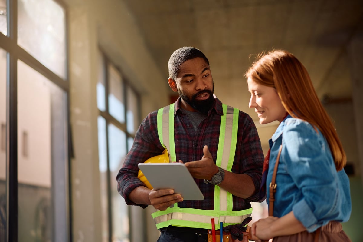 African American construction worker and female homeowners using using digital tablet while stalking about house renovation details. Copy space.